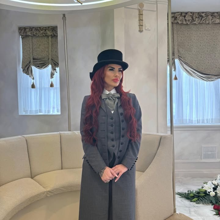 A Butterflies Rising funeral director in a grey tailcoat, waistcoat, bow tie and top hat, standing in the parlour